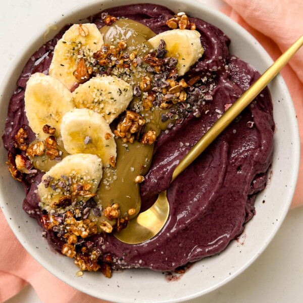 white bowl of acai with banana, granola and sunflower butter on top