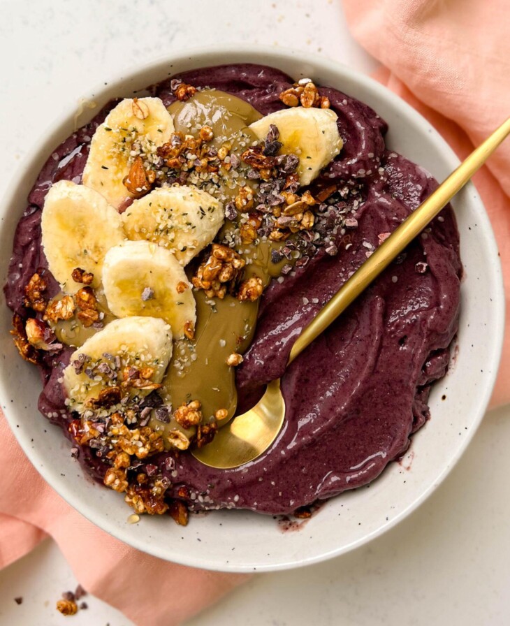 white bowl of acai with banana, granola and sunflower butter on top