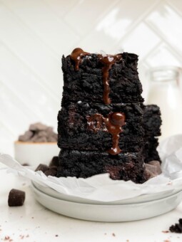 vegan brownies stacked on a white plate next to a bottle of milk and a bowl of chocolate chips