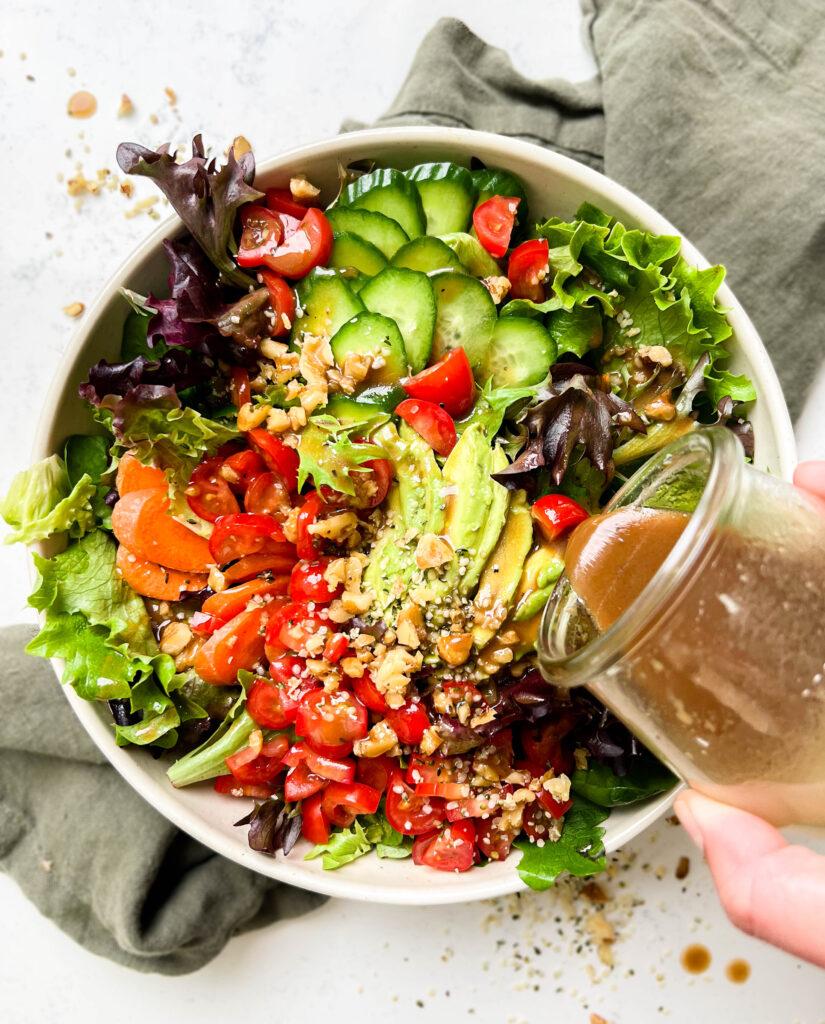classic garden salad with tomatoes, carrots, avocado, greens and nuts in a bowl on a green linen cloth