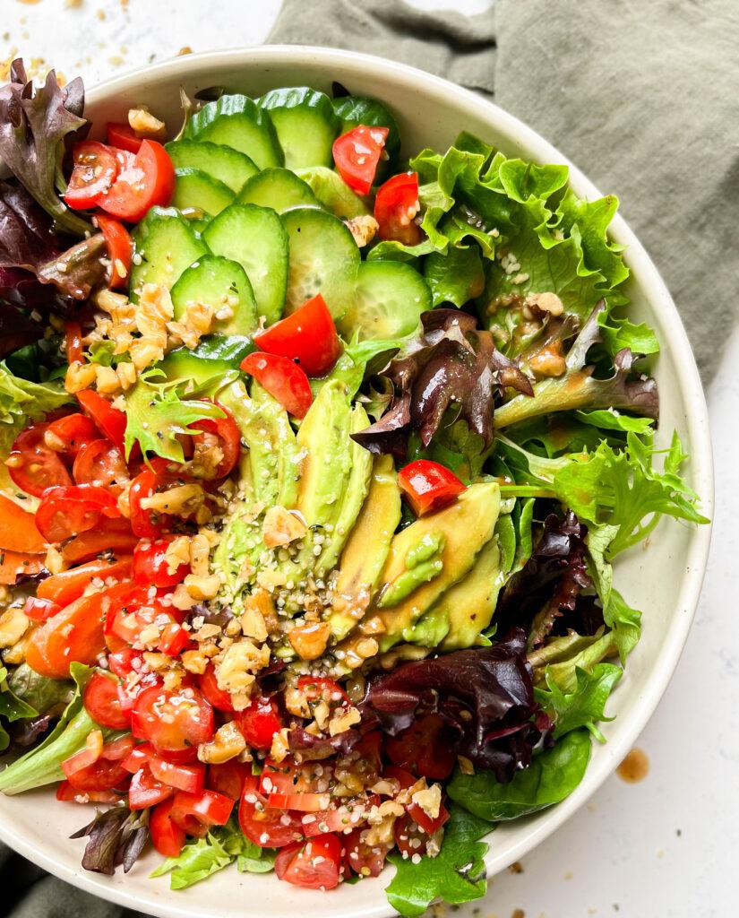 classic garden salad with tomatoes, carrots, avocado, greens and nuts in a bowl on a green linen cloth