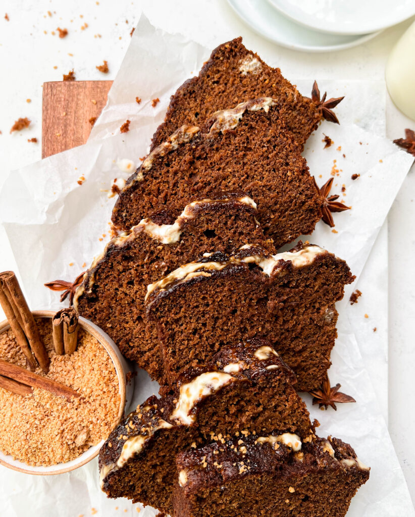 vegan gingerbread loaf slices on parchment paper next to a bowl of coconut sugar and white plates