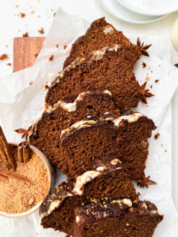 vegan gingerbread loaf slices on parchment paper next to a bowl of coconut sugar and white plates