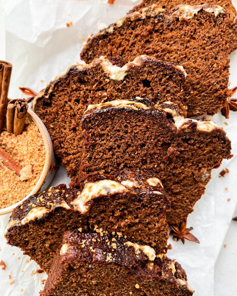 vegan gingerbread loaf slices on parchment paper next to a bowl of coconut sugar and white plates