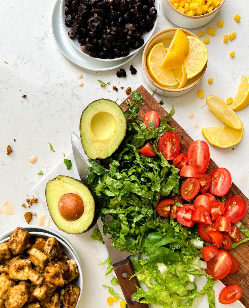 avocado, tomatoes, corn, black beans and tofu spread out on a cutting board with lettuce