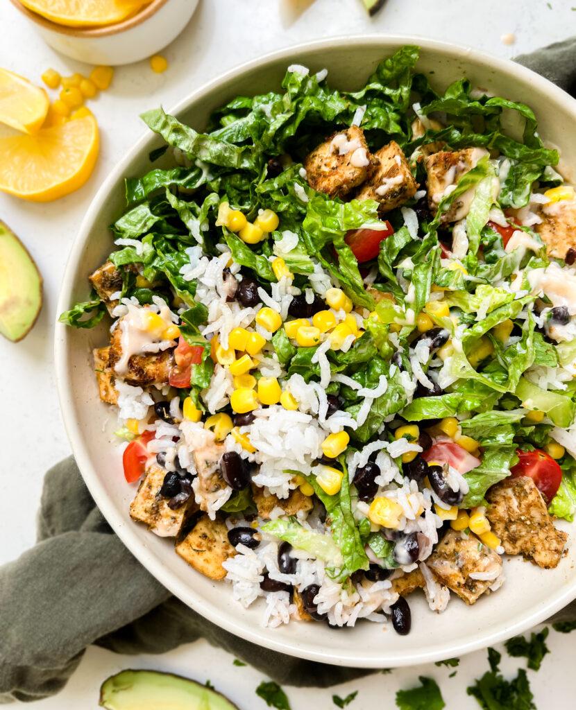 vegan chipotle burrito bowl on a green linen cloth next to lemon wedges and avocado