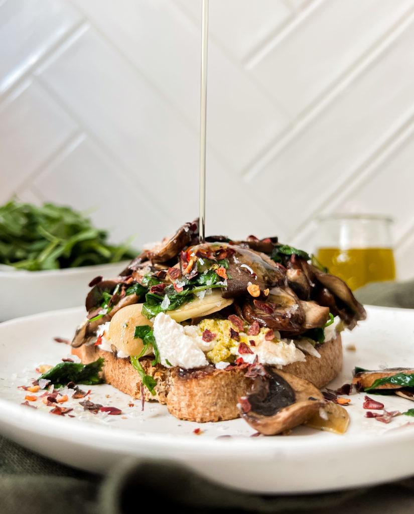 toast with mushrooms and ricotta on a white plate with oil poured on top