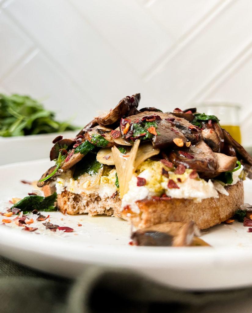 toast on a white plate with oil poured on top next to a bowl of greens