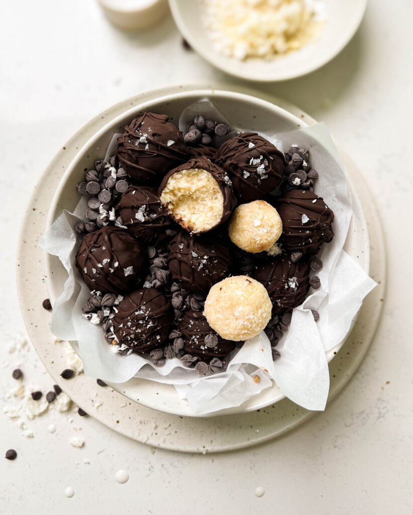 bounty balls in a white bowl next to a glass of milk and a bowl of shredded coconut