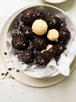 bounty balls in a white bowl next to a glass of milk and a bowl of shredded coconut