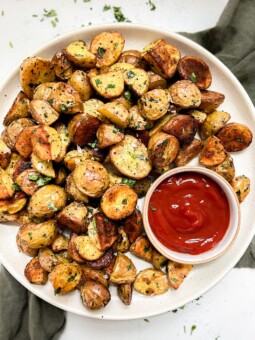 crispy oven baked potatoes on a beige plate next to a bowl of ketchup