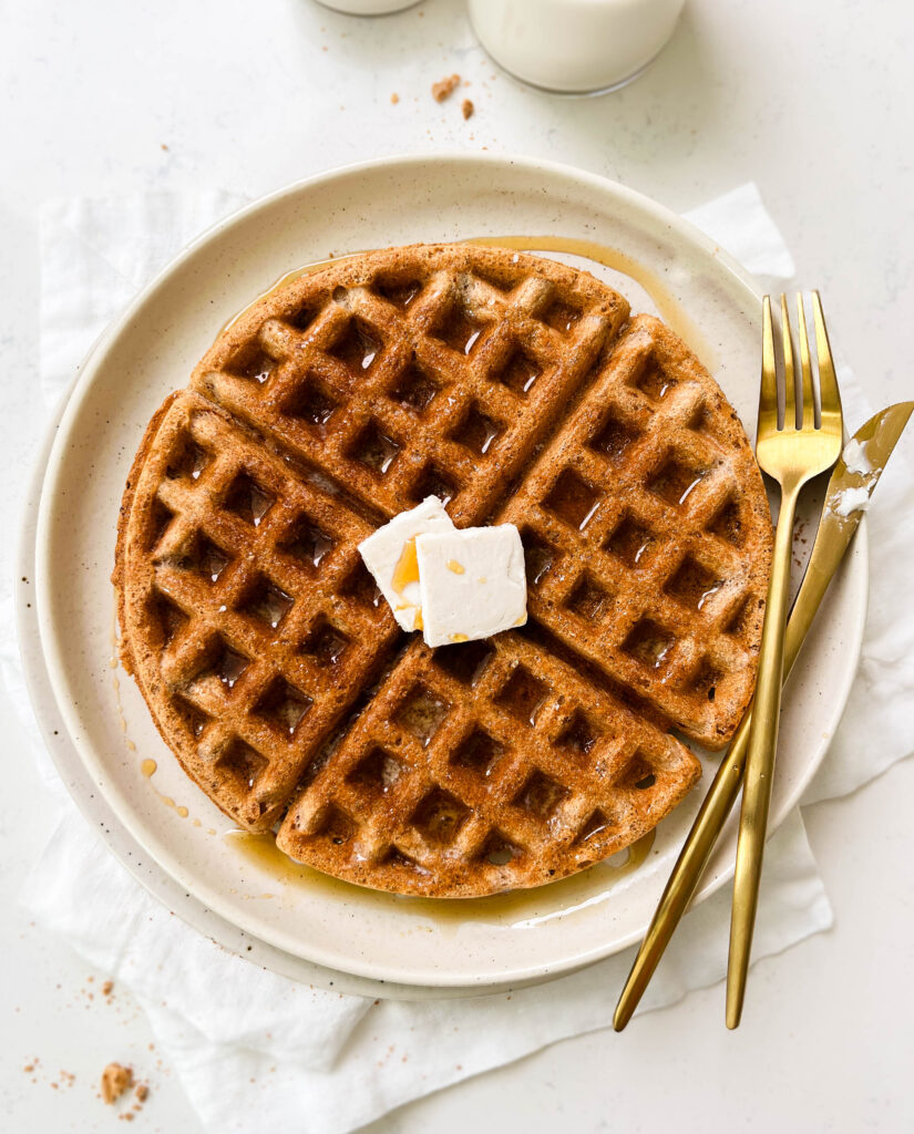 vegan waffle on a beige plate next to a glass of milk