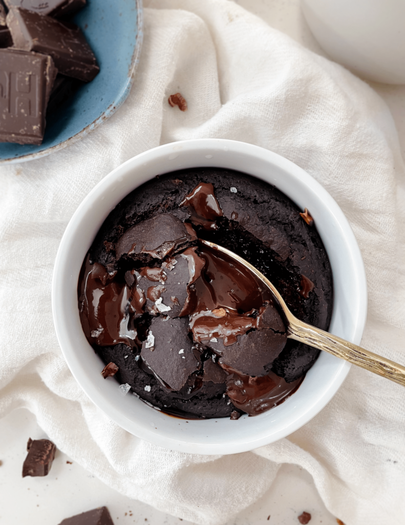brownie in a mug next to a bowl of chocolate