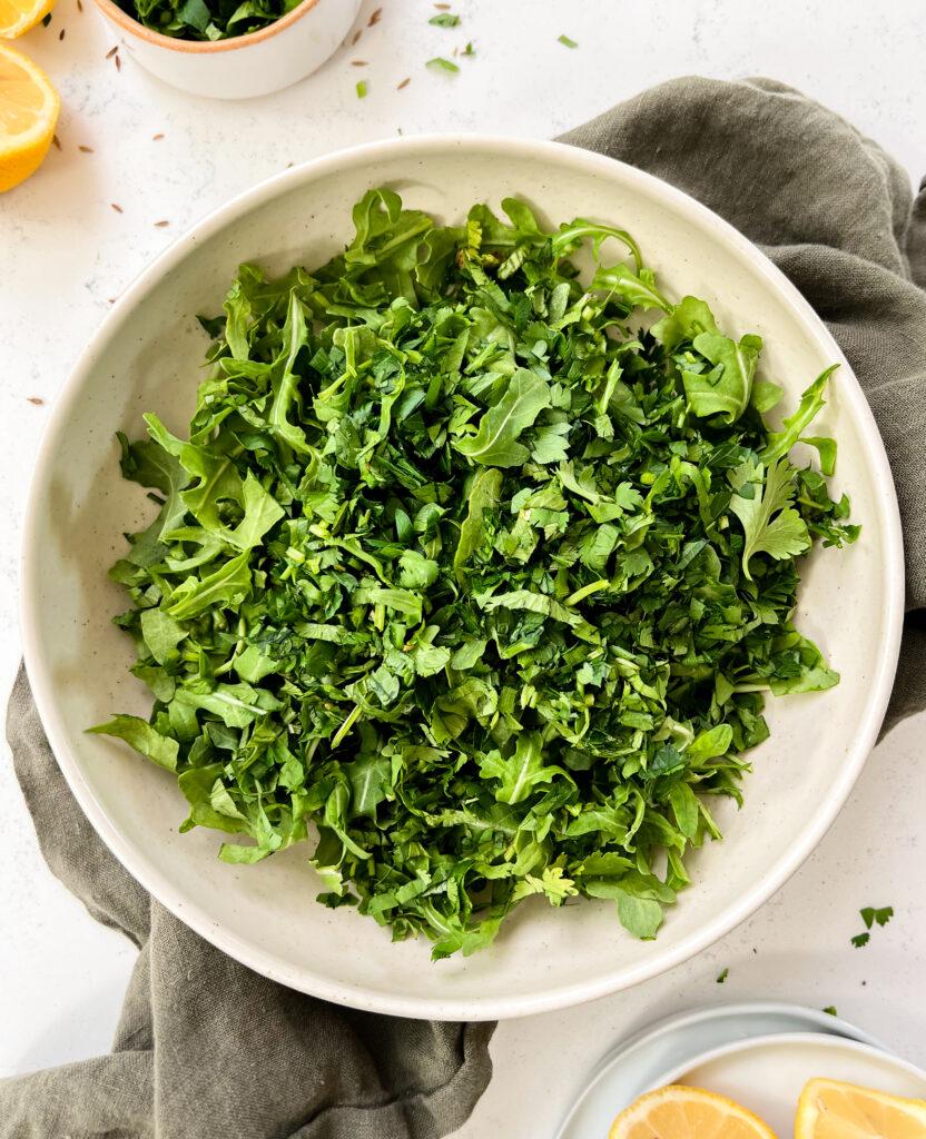 arugula in a beige bowl next to cut lemons