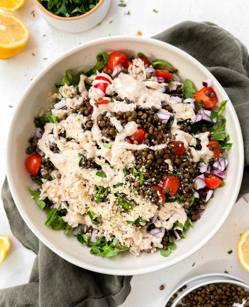 spicy vegan lentil salad with tahini dressing in a beige bowl on a green linen napkin next to lemons