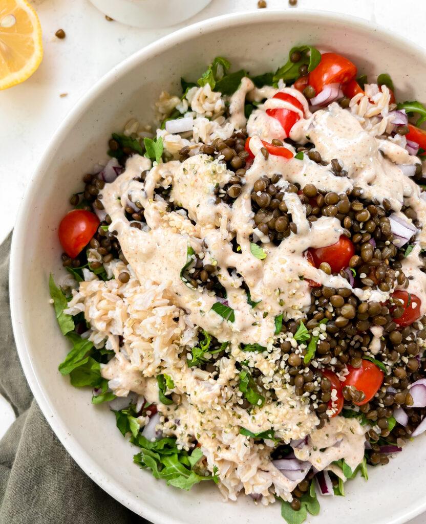 spicy vegan lentil salad with tahini dressing in a beige bowl on a green linen napkin next to lemons