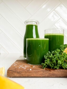 easy green juice in a jar and two glasses on wooden cutting board next to kale and lemons