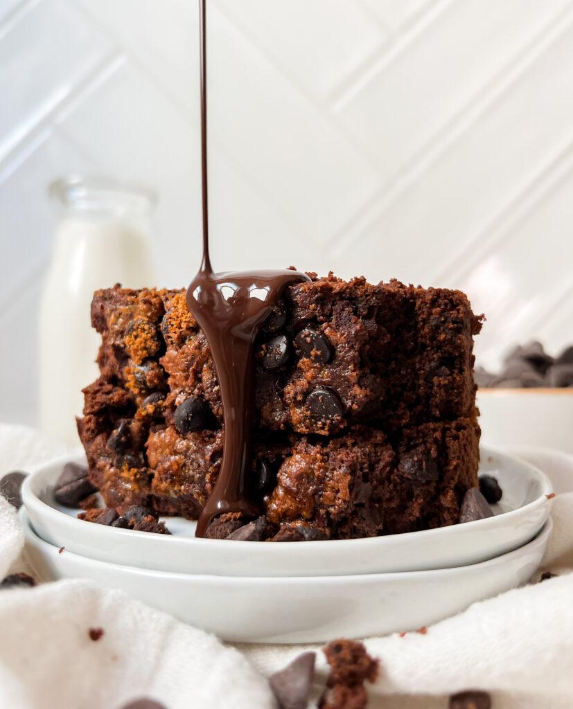 vegan chocolate pumpkin bread slices stacked on a white plate with syrup poured on top
