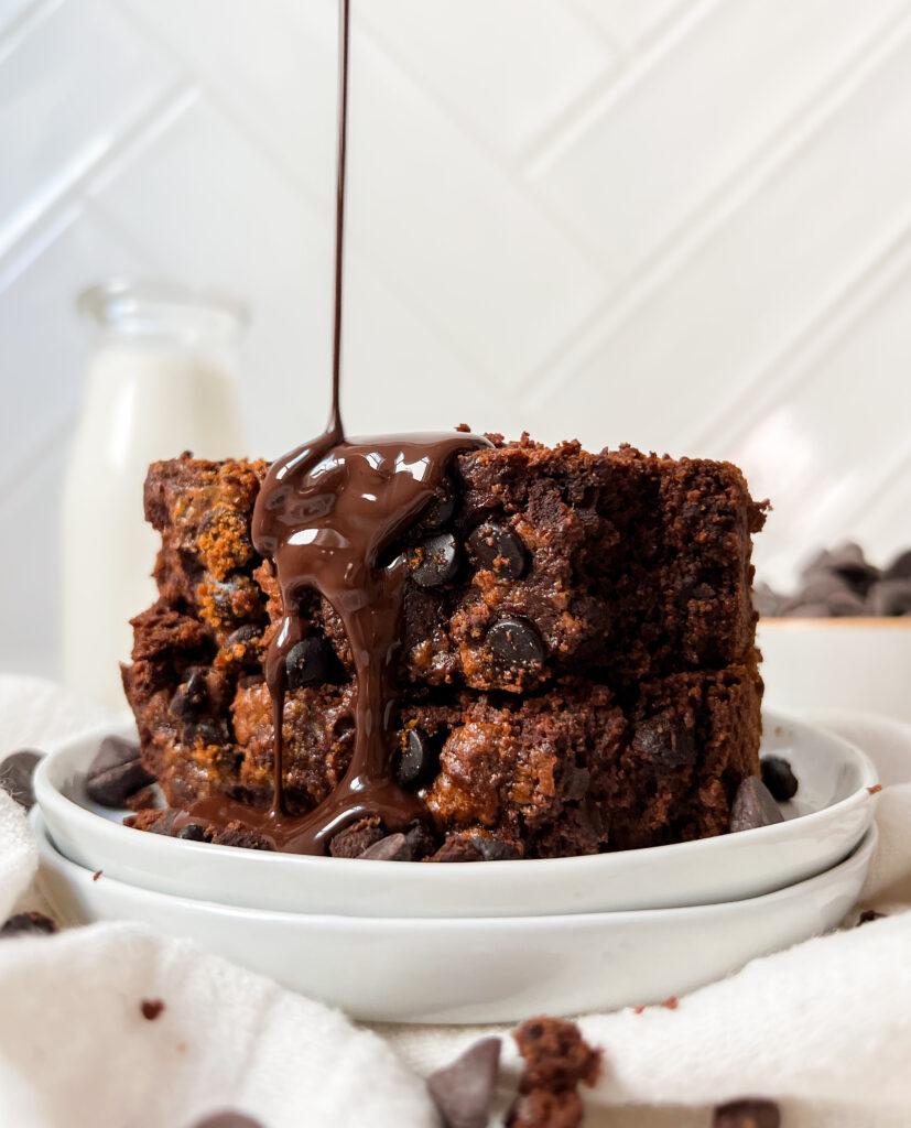 vegan chocolate pumpkin bread slices stacked on a white plate with syrup poured on top