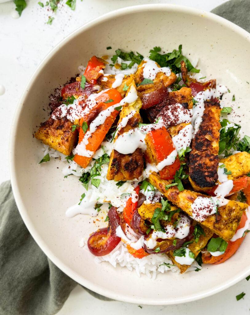 vegan shawarma bowl with middle eastern tofu, veggies and yogurt sauce on top