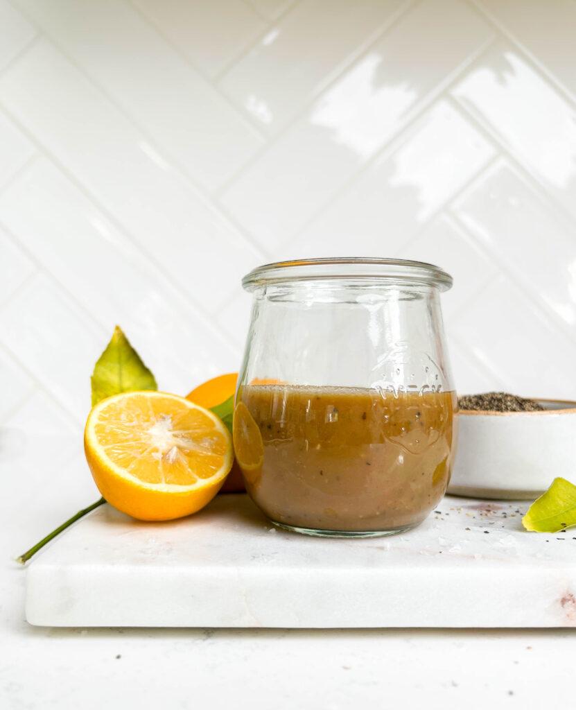 creamy balsamic vinaigrette dressing in a jar on a cutting board next to lemons