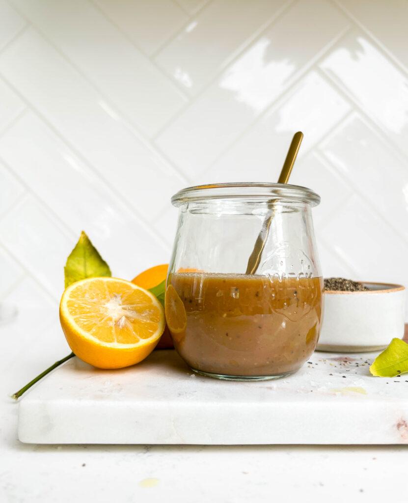 creamy balsamic vinaigrette dressing in a jar on a cutting board next to lemons