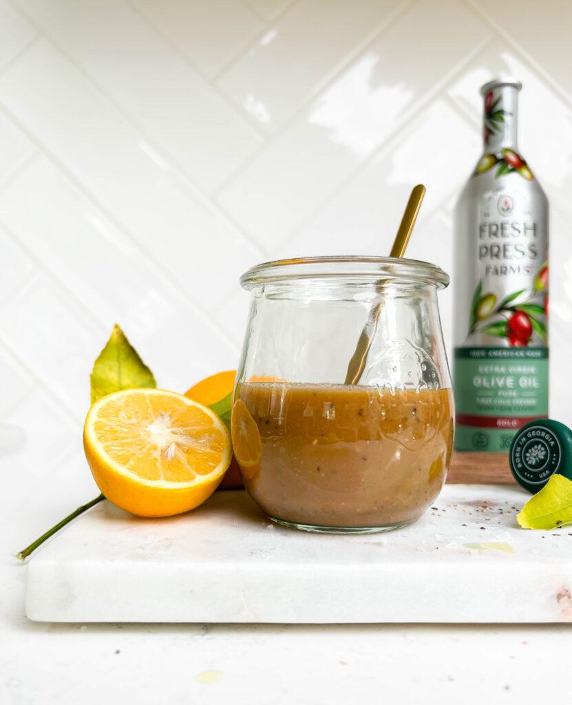 creamy balsamic vinaigrette dressing in a jar on a cutting board next to lemons and Fresh Press Farms olive oil