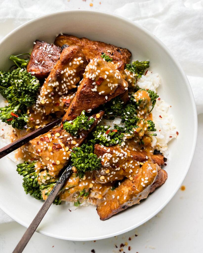 marinated peanut tempeh with white rice and broccoli next to a white linen cloth