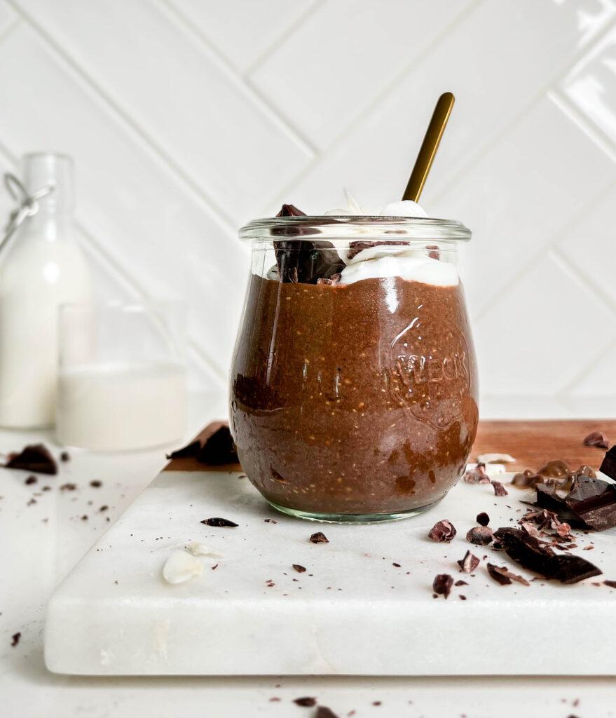 healthy chocolate seed pudding in a jar on a white cutting board next to chocolate and jar of milk
