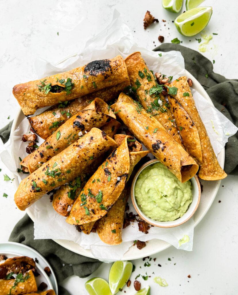 crispy baked vegan taquitos next to avocado crema sauce