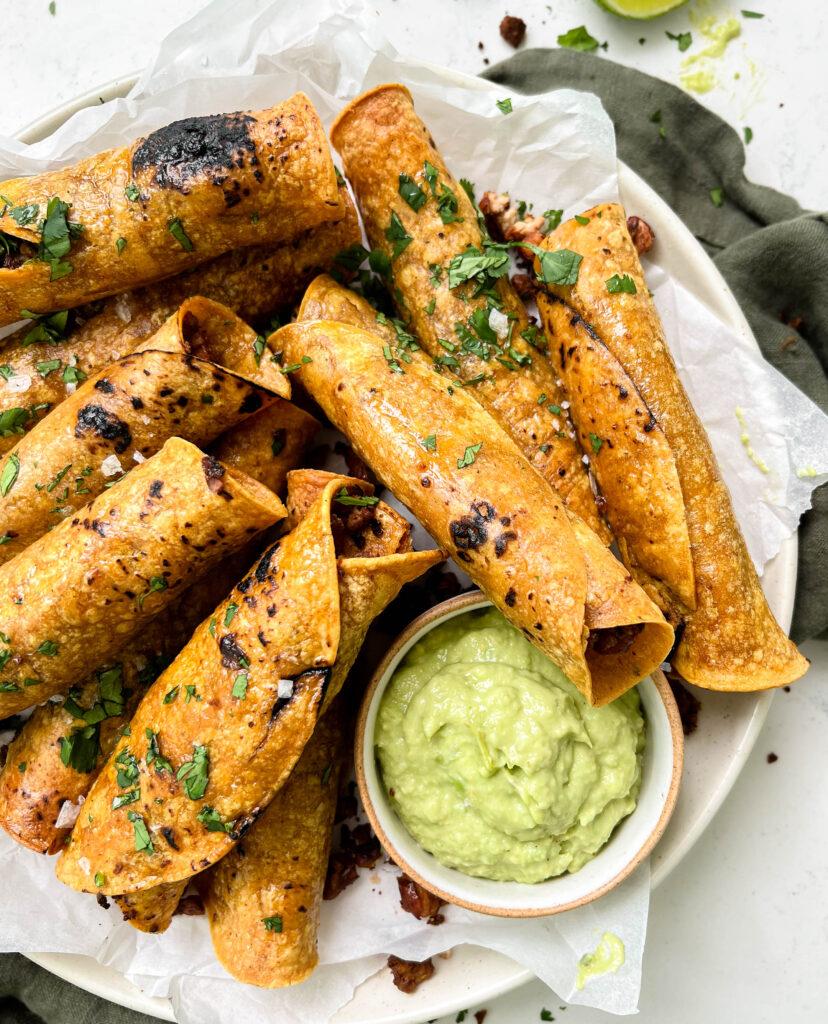 crispy baked vegan taquitos next to avocado crema sauce
