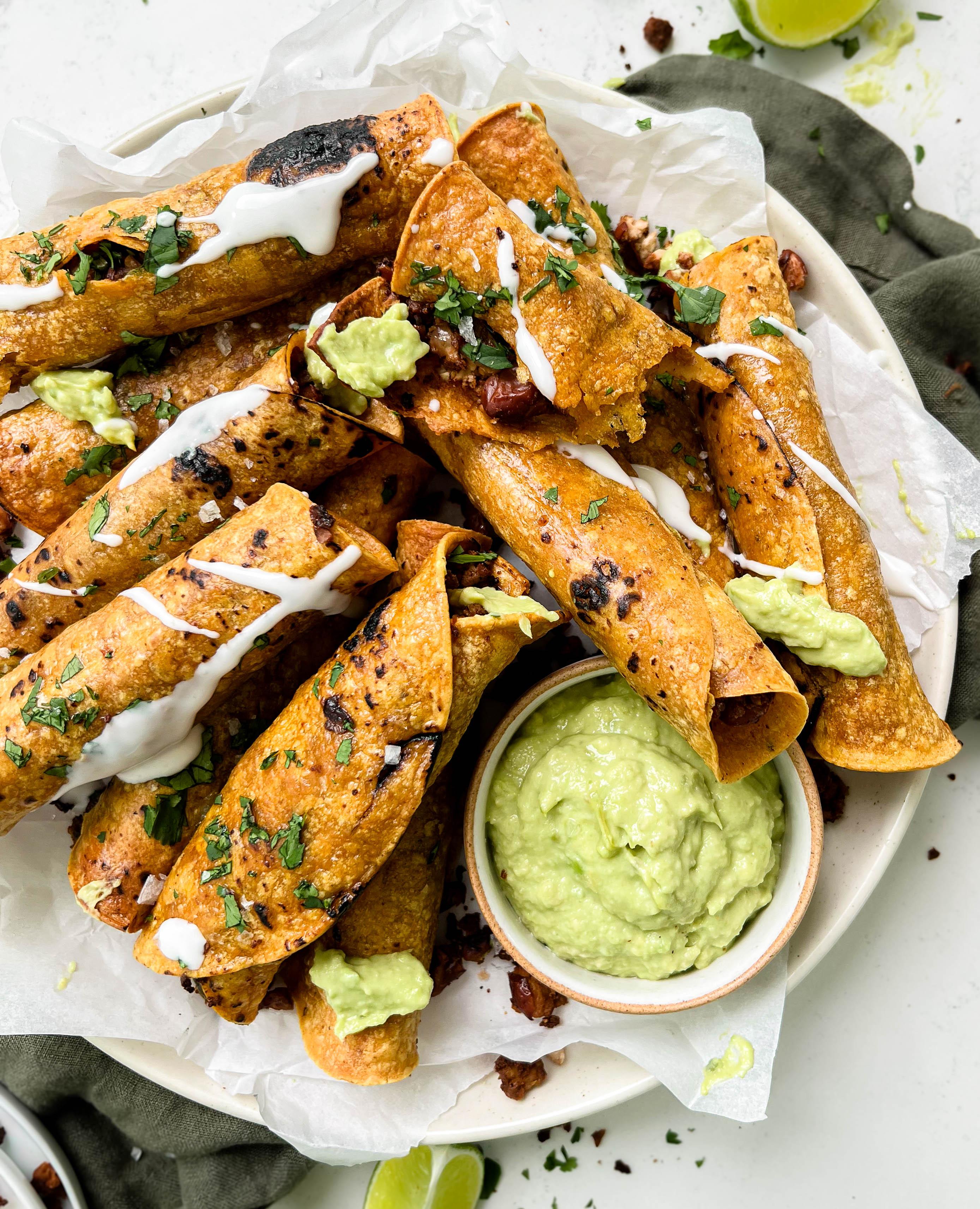 crispy baked vegan taquitos next to avocado crema sauce