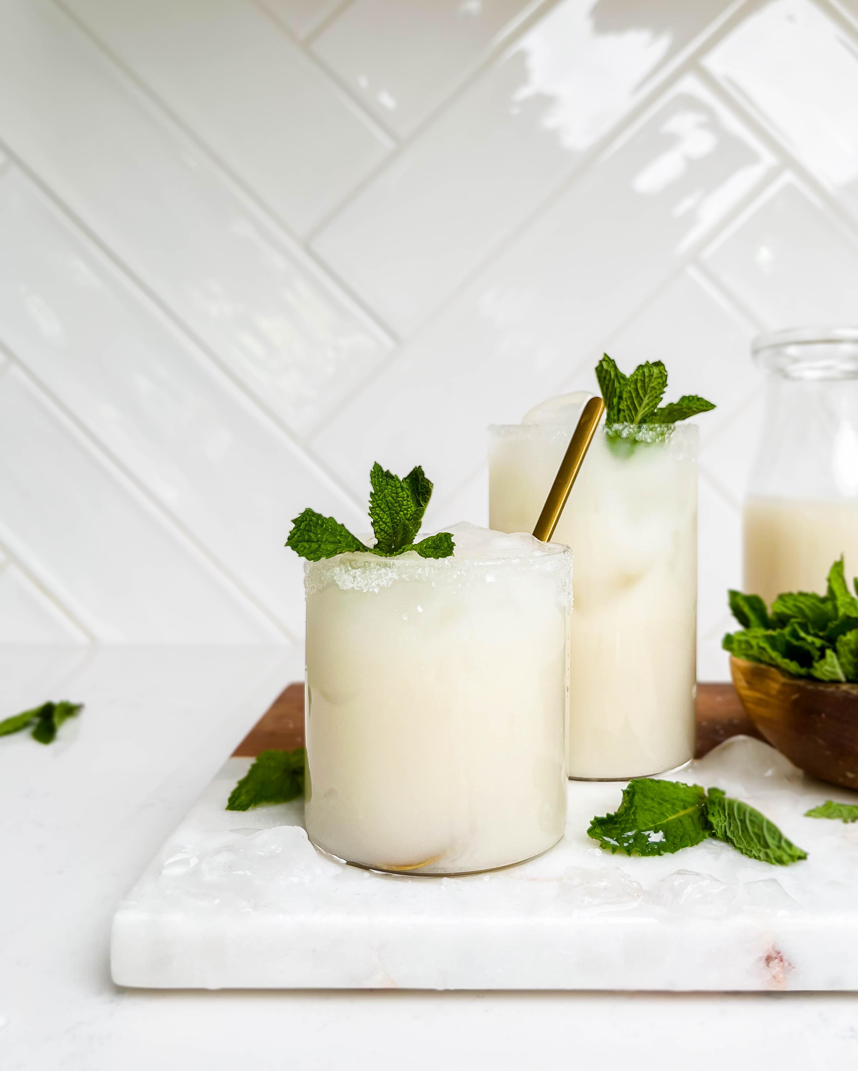 two glasses of coconut lemonade on a marble and wood cutting board