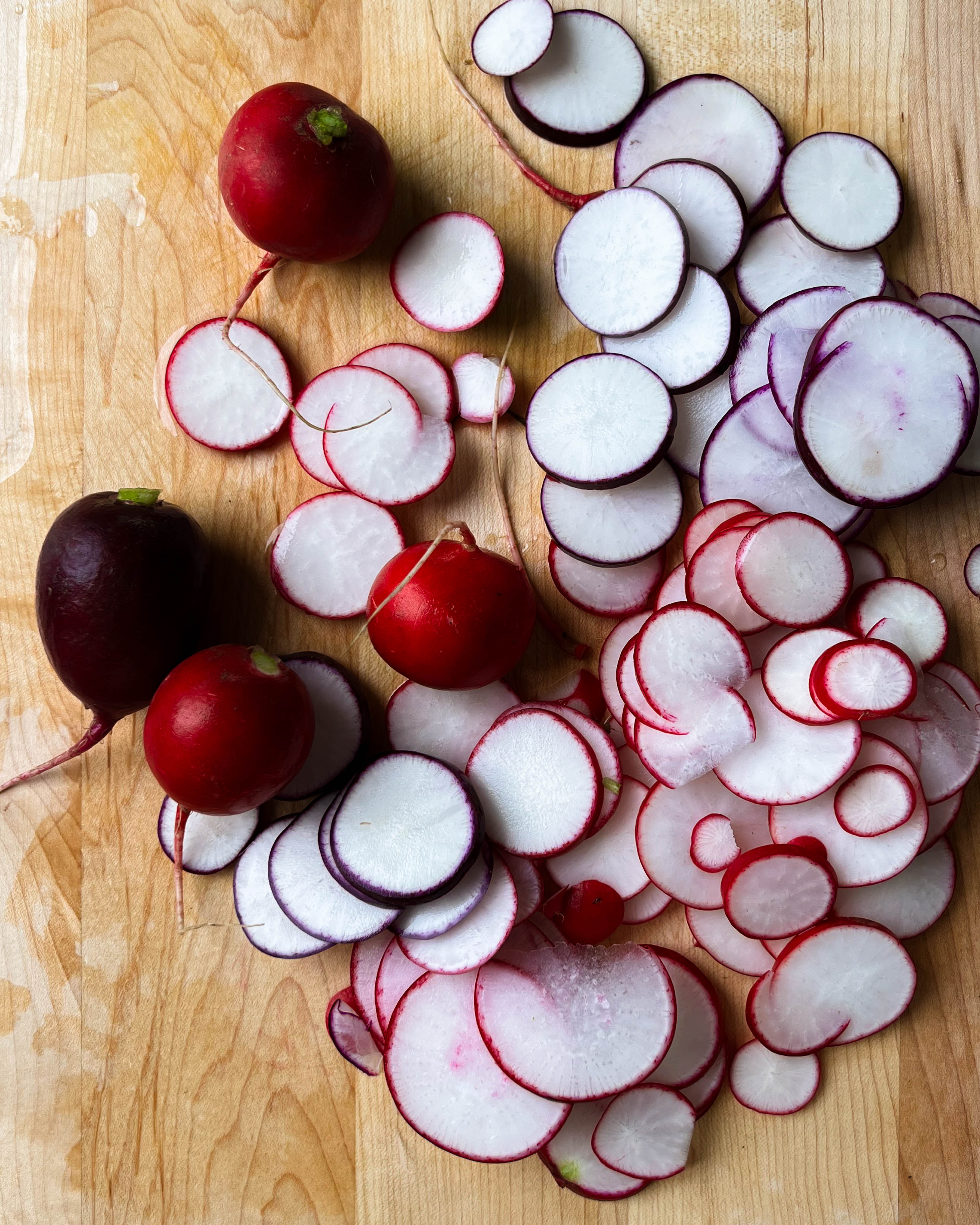 thinly sliced radishes on a wooden cutting board